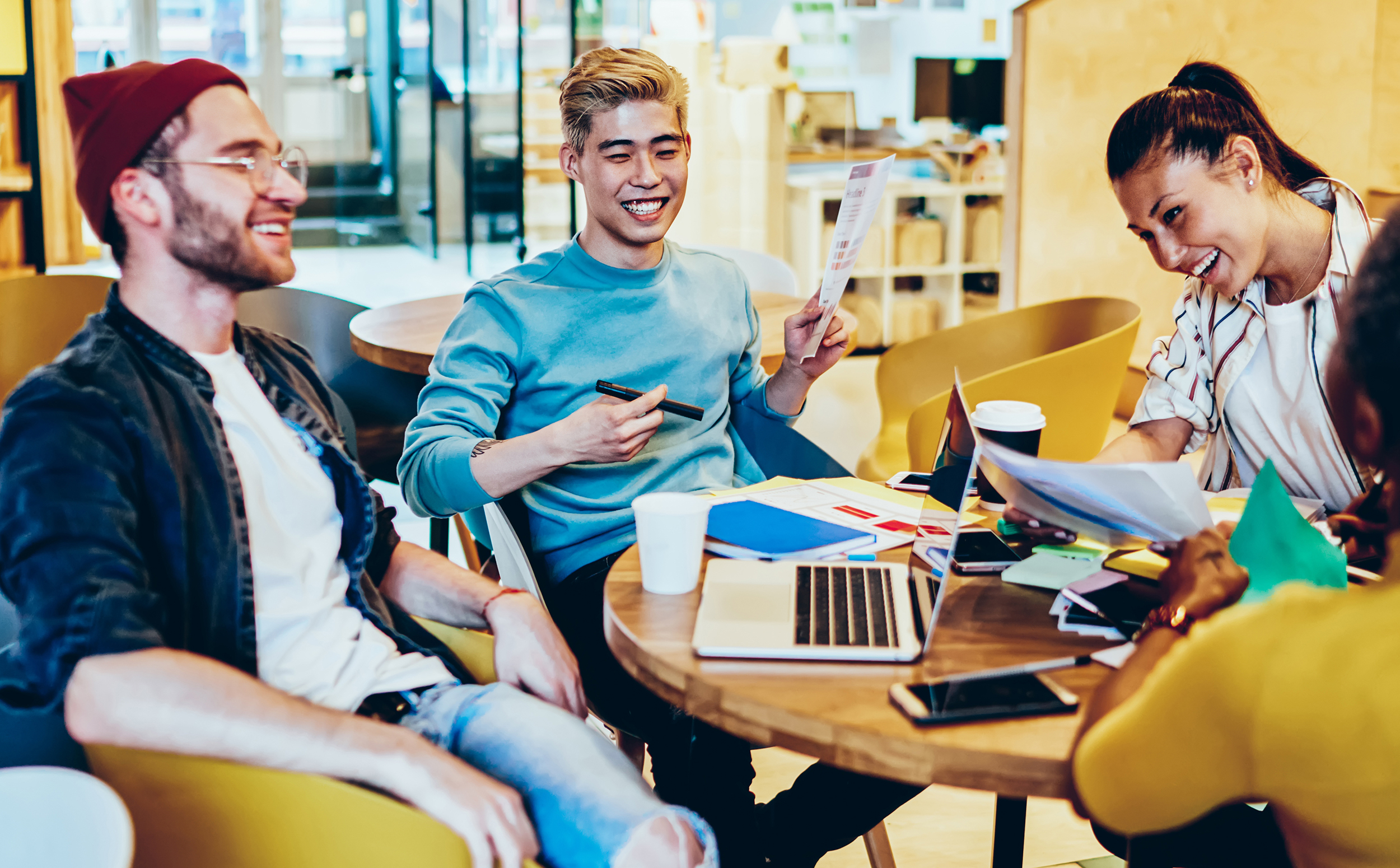 smiling multiracial crew sitting at desktop laughing and doing homework